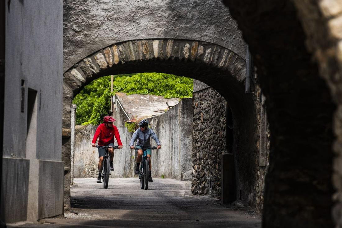 Two riders cycling under a stone archway